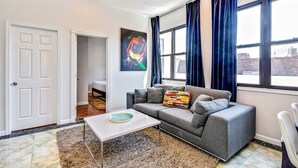 A modern living room with a grey sofa, a white coffee table, and a colorful abstract painting on the wall.