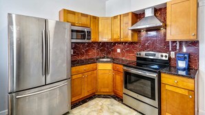 A kitchen with stainless steel appliances, wooden cabinets, a marble backsplash, and a built-in oven.