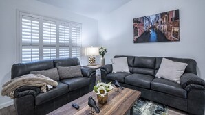 A living room with two dark leather sofas, a coffee table, and a painting of a canal.
