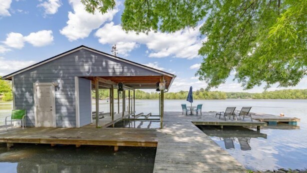 Una baita sul lago con un pontile che si protende nell'acqua, un'area relax coperta e un piccolo tavolo da esterno.