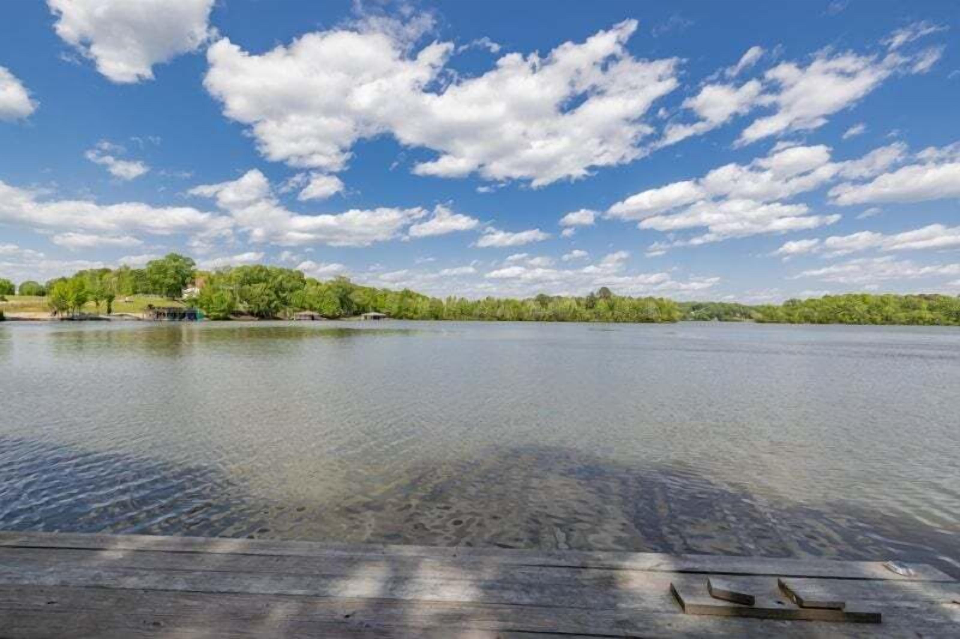 Ein ruhiger See mit einer Holzsteganlage, umgeben von Bäumen und einem klaren Himmel.