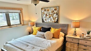 A bedroom with a bed, bedside tables, a ceiling fan, a window, and a wall art piece. - Long Lake Retreat in Phillips, Wisconsin (Phillips)