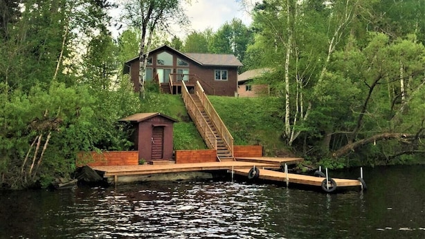 A house on stilts over water with a wooden dock and stairs leading to the entrance. - Long Lake Retreat in Phillips, Wisconsin (Phillips)