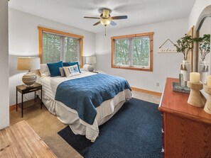 A bedroom with a bed, two bedside tables, a ceiling fan, and two windows with blinds.