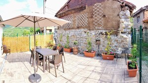 Une terrasse extérieure avec une table et des chaises, entourée de plantes en pot et d’un mur de pierre.
