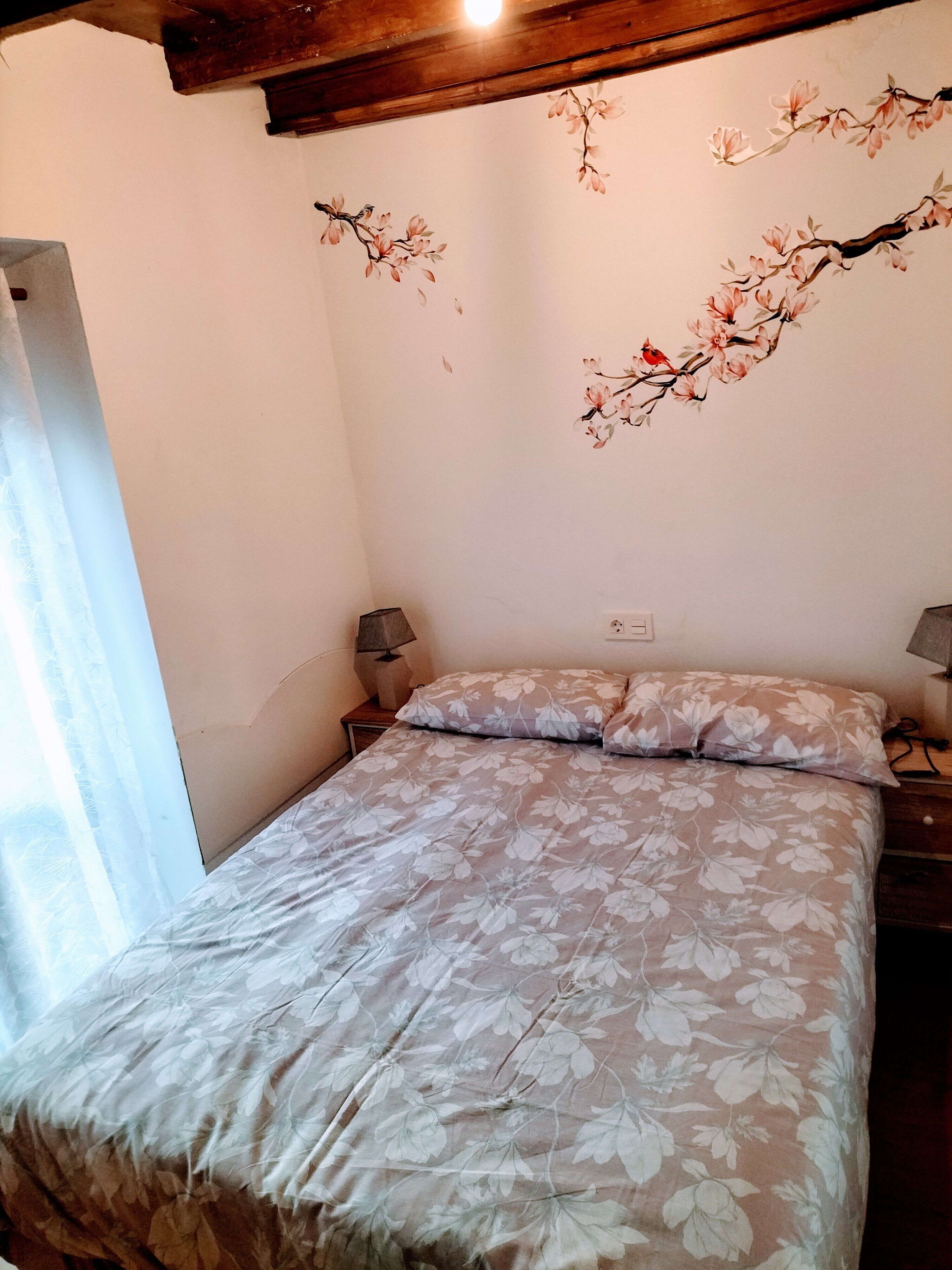 Une chambre à coucher avec une couvre-lit à motifs floraux, un plafond en bois et une fresque murale représentant des fleurs de cerisier.