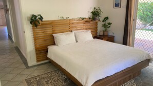 A bedroom with a wooden headboard, a bed with white bedding, two bedside tables with potted plants, and a patterned rug on the floor. - 26 Tambor Drive - Pool and Pet Friendly (Exmouth)