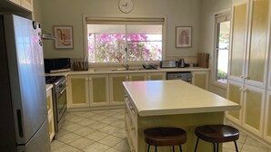 A kitchen with a refrigerator, stove, sink, and a window with pink flowers outside. - 26 Tambor Drive - Pool and Pet Friendly (Exmouth)