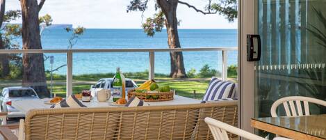 A balcony with wicker furniture, a table with breakfast items, and a view of the sea.
