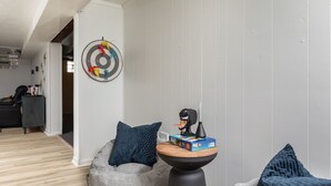 A modern living room with a grey bean bag chair, a small round table with a decorative item, and a dartboard on the wall. - Parma Home w/ Hot Tub and Arcade Room! (Parma)