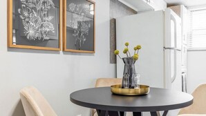 Een eethoek met een ronde tafel, twee ingelijste kunstwerken aan de muur, en een vaas met gele bloemen op een messing dienblad.
