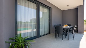 Un área de comedor exterior moderna con una mesa y sillas, una planta en maceta y un ventanal corredizo que da a un balcón.