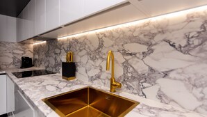 Una cocina moderna con salpicadero de mármol, un lavabo dorado y una cafetera negra.