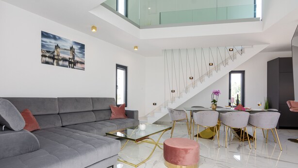 Una sala de estar moderna con un sofá gris, una mesa de centro de vidrio y una escalera que lleva a un nivel superior.