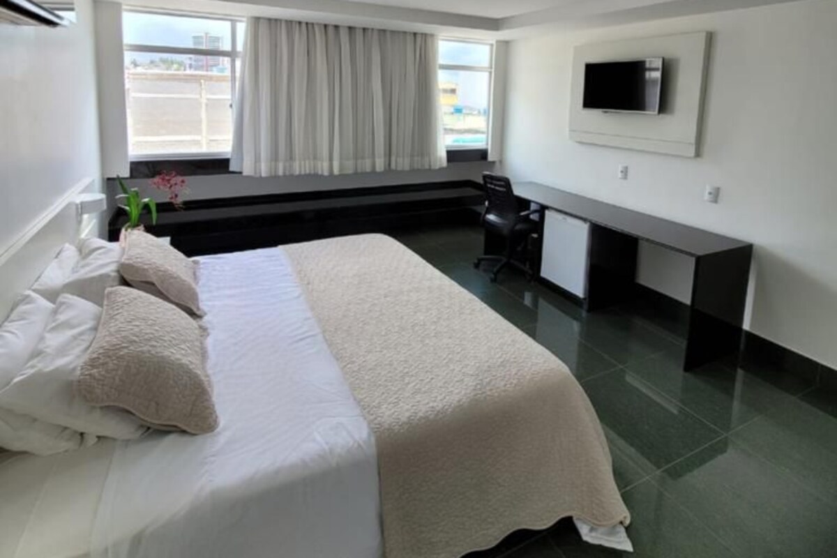Hotelkamer met een bed, bureau, stoel, een aan de muur bevestigde televisie en een raam met gordijnen.