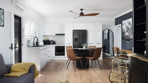 Una cocina moderna con armarios blancos, un refrigerador negro y una zona de comedor con una mesa redonda y sillas.
