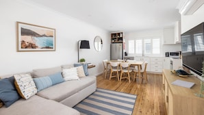 Un appartement moderne comprenant un salon, un coin repas, une cuisine et une grande fenêtre équipée de stores.