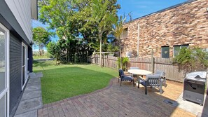 Un patio trasero con césped, una cerca de madera, una parrilla y mobiliario exterior.
