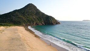 Una playa con una gran colina al fondo y una vista despejada del océano.