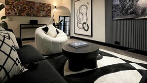 A modern living room with a black and white sofa, a round coffee table, and a large abstract painting on the wall. - Elegant 2-bed Oasis: Renovated, Artful Decor & Sunlit in Queens Park (London)