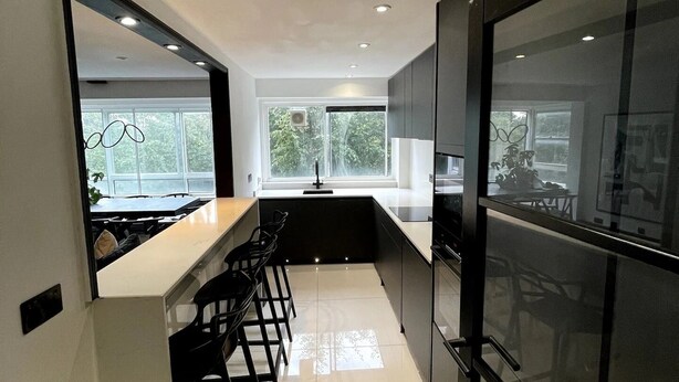A modern kitchen with a central island, bar stools, and large windows. - Elegant 2-bed Oasis: Renovated, Artful Decor & Sunlit in Queens Park (London)