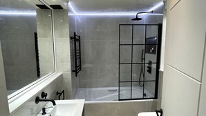 A modern bathroom with a large mirror, a bathtub, and a toilet. - Elegant 2-bed Oasis: Renovated, Artful Decor & Sunlit in Queens Park (London)