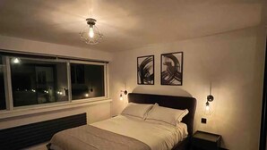 A modern bedroom with a large bed, bedside lamps, and abstract wall art. - Elegant 2-bed Oasis: Renovated, Artful Decor & Sunlit in Queens Park (London)