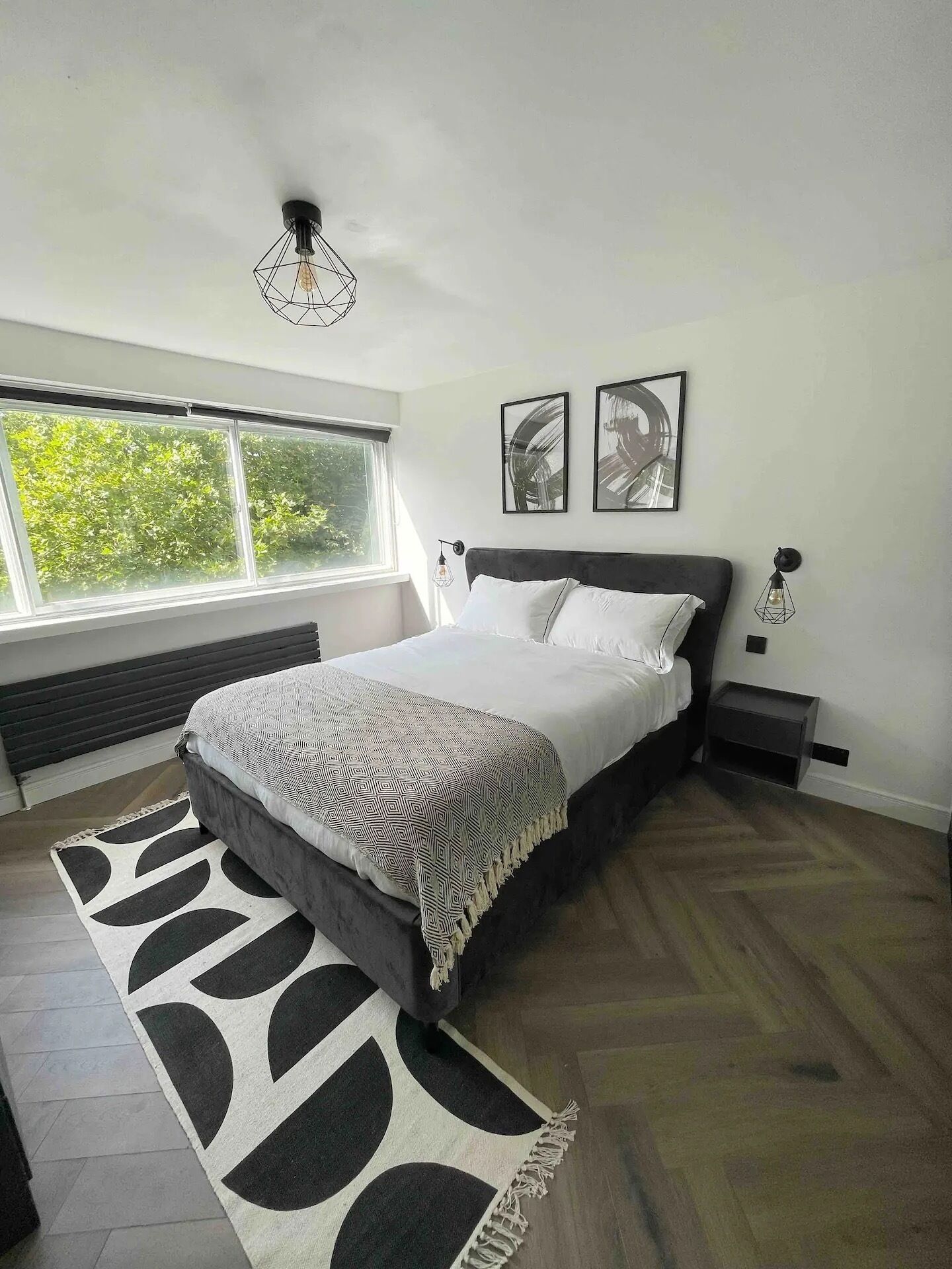 Een moderne slaapkamer met een groot bed, een raam met uitzicht op groen en twee kunstwerken aan de muur.