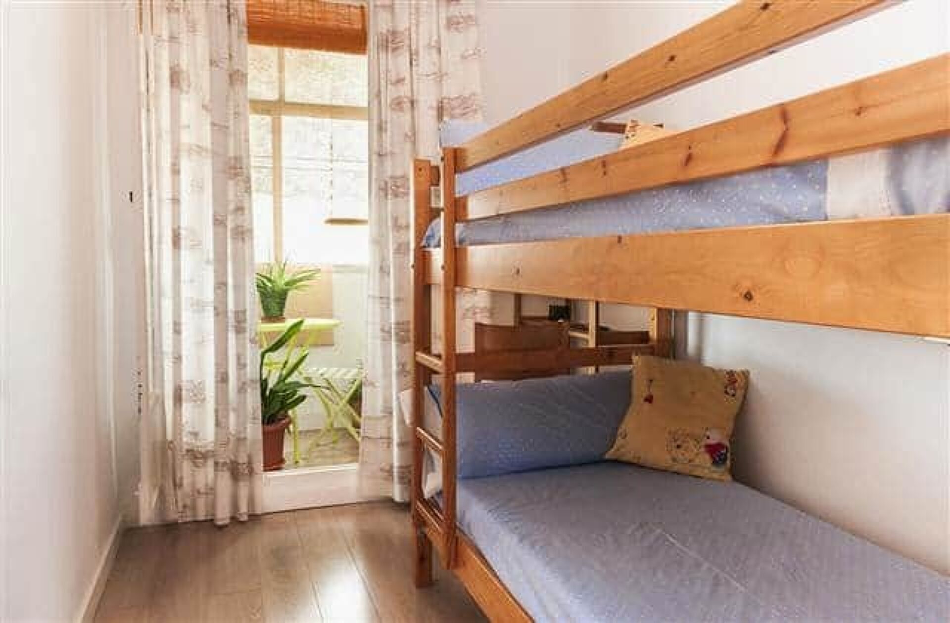 A bunk bed room with a window, curtains, and a potted plant.