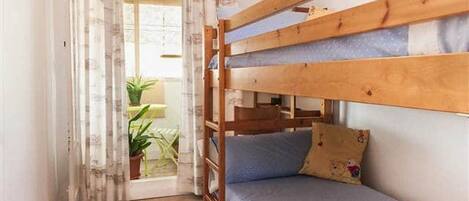 A bunk bed room with a window, curtains, and a potted plant.