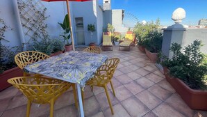 Eine Terrasse mit Tisch und Stühlen, umgeben von Kübelpflanzen und einem roten Sonnenschirm.