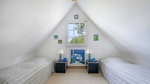 Una piccola camera mansardata a forma di triangolo con due letti, due comodini, una finestra e un quadro appeso al muro.