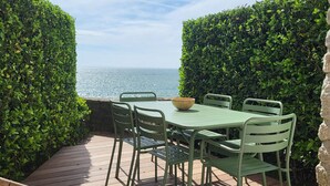 Une terrasse en bois avec une table et des chaises, un saladier et un fauteuil en osier.
