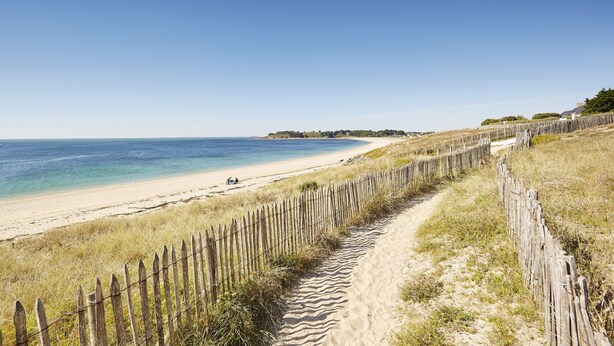 Une plage de sable bordée d’une clôture en bois, sous un ciel bleu et dégagé.