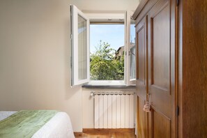 Ein Schlafzimmer mit Fenster, Holzschrank, Heizkörper und einem Bett mit grüner Decke.