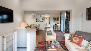 Un salon avec un canapé, une table basse sur laquelle sont posés des livres, un téléviseur et un lustre.