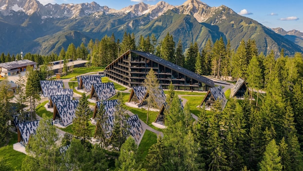 Un albergue de montaña con varias cabañas, un edificio central amplio y montañas nevadas al fondo.