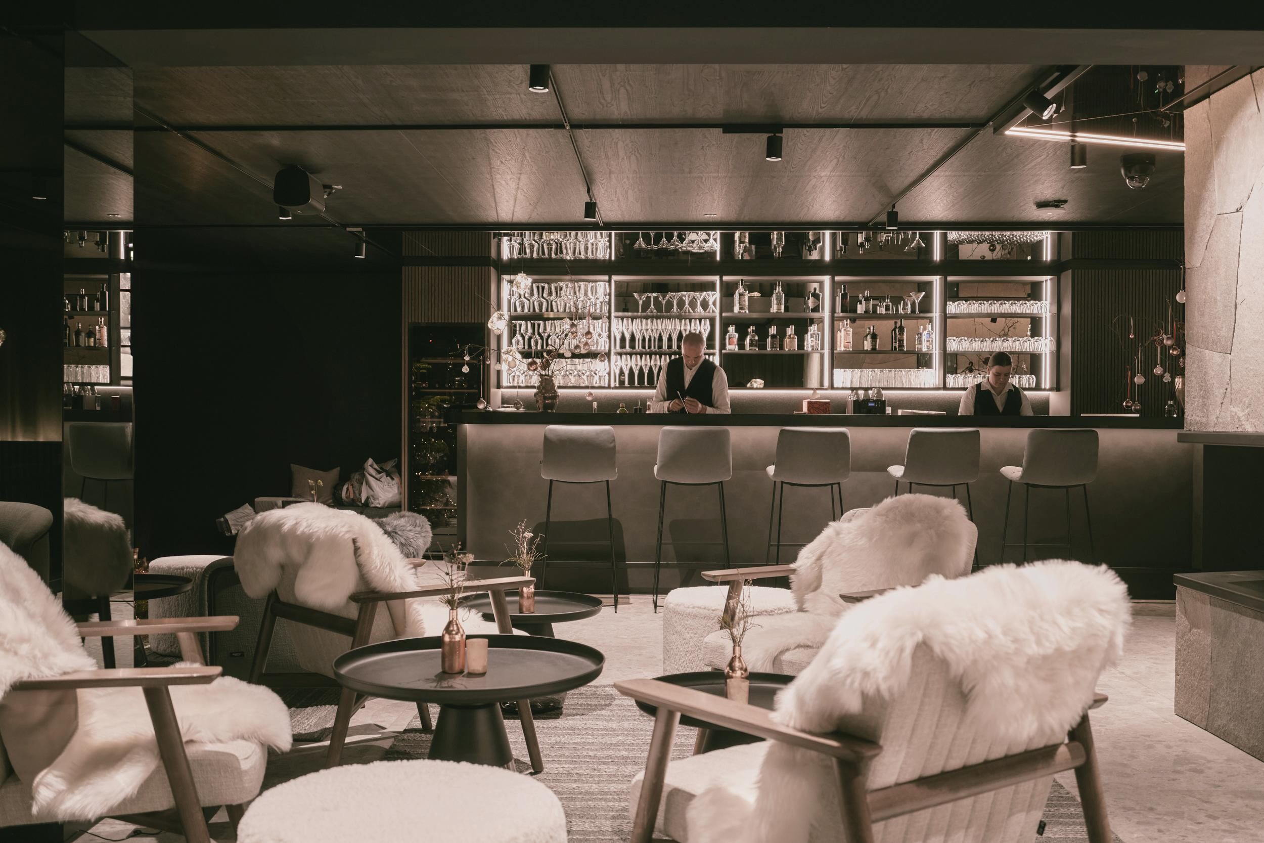 A bar area with a bartender, round tables, and chairs.