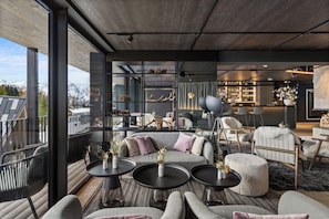 A modern interior with a sofa, round tables, and a bar area. - TRIFORET alpin.resort by Falkensteiner (Hinterstoder)