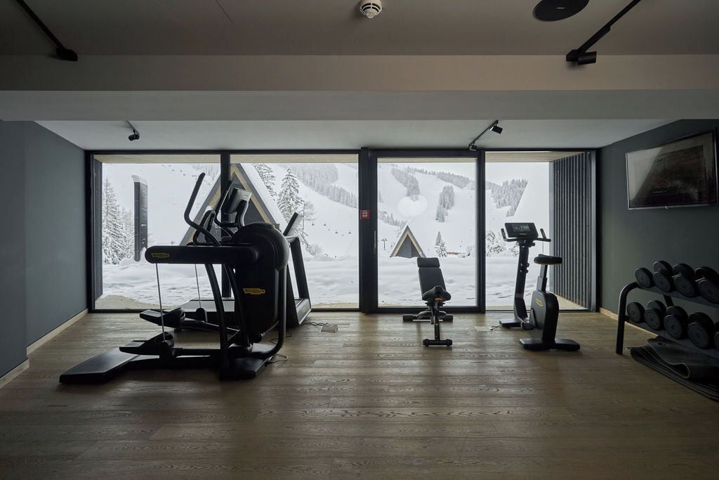 Ein Fitnessraum mit Trainingsgeräten, großen Fenstern und Blick auf eine verschneite Landschaft.