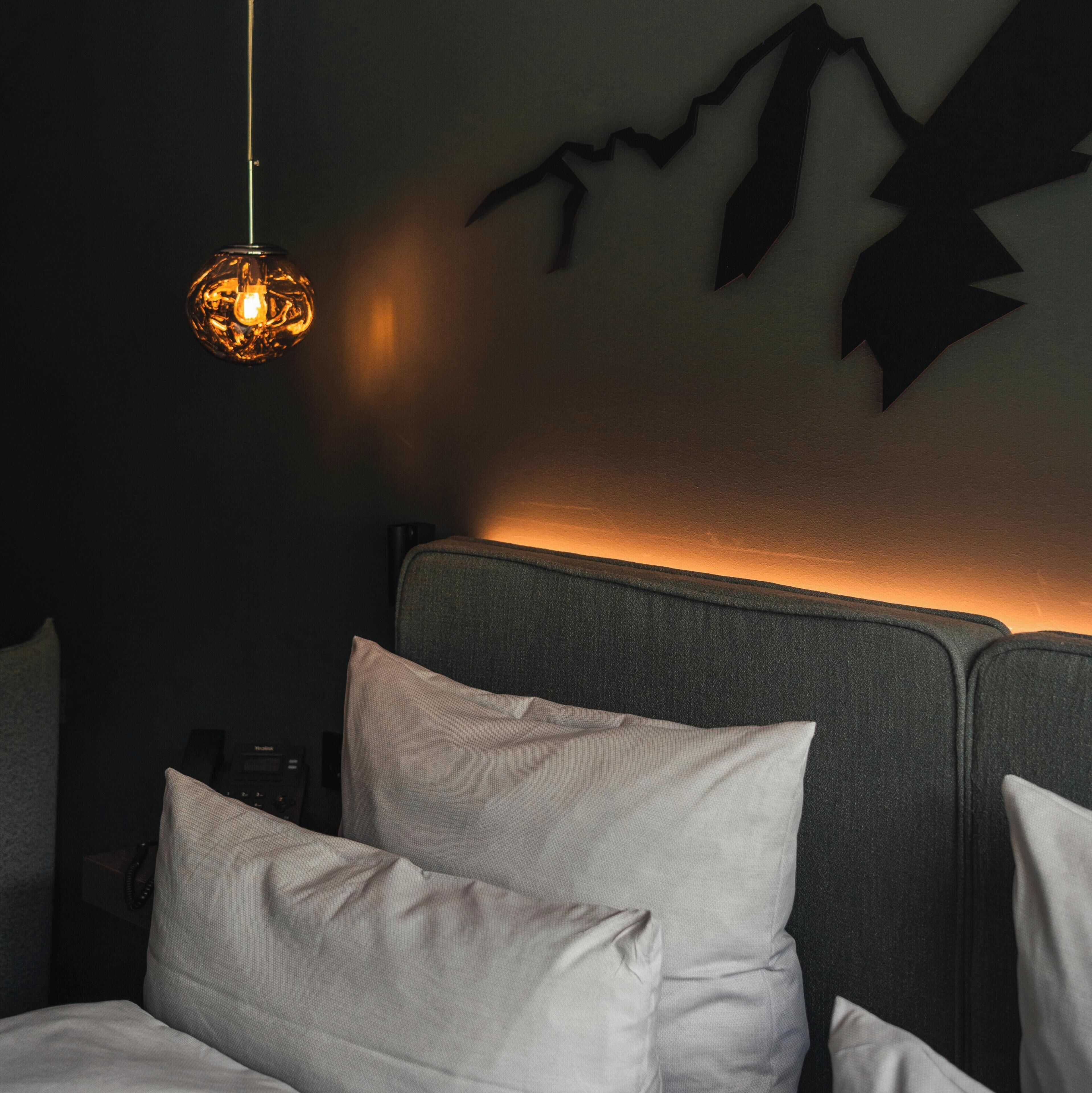 A bedroom with a bed, pillows, a wall-mounted light fixture, and a wall decoration.