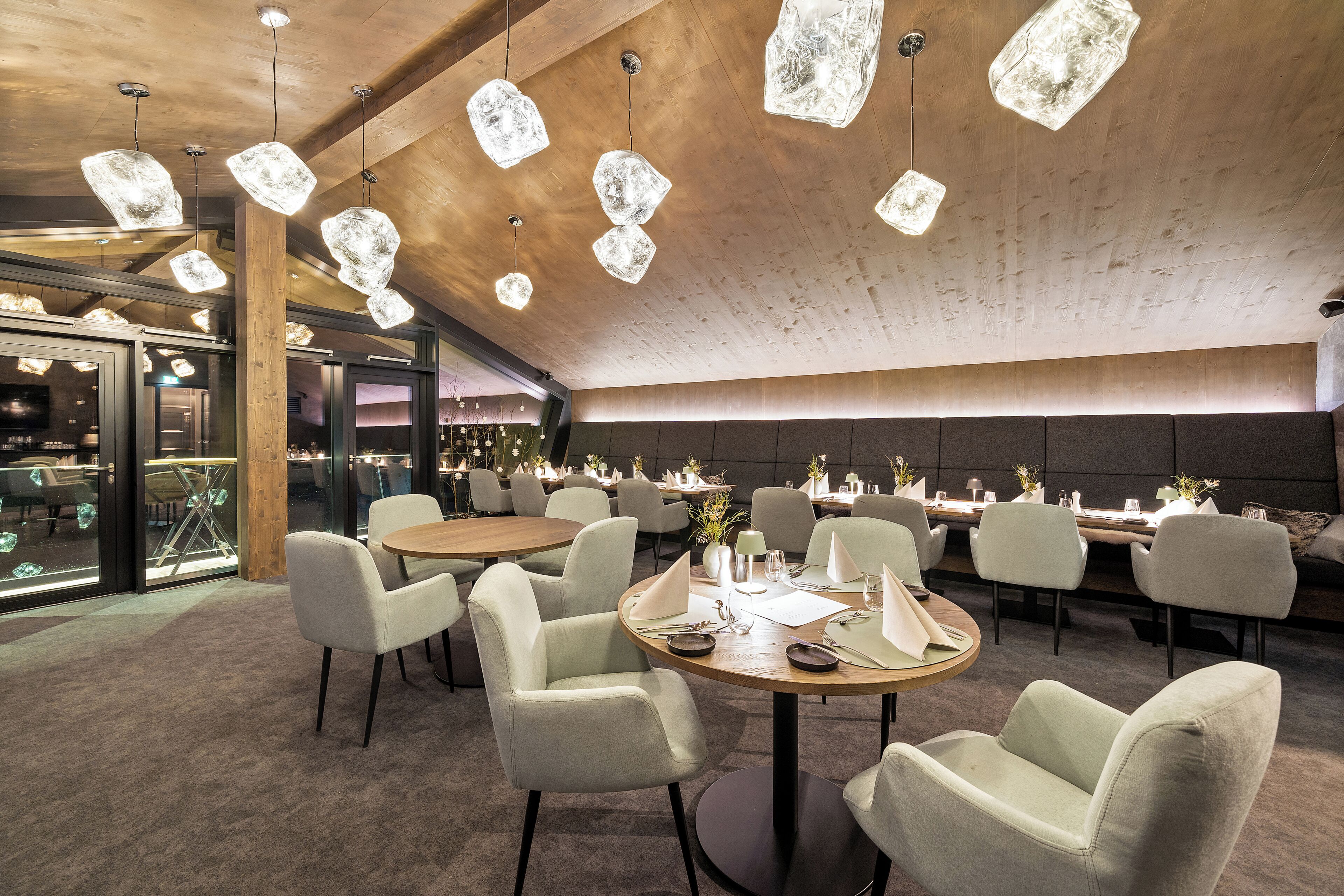 Un restaurant moderne avec des tables rondes, des chaises rembourrées et des luminaires suspendus.