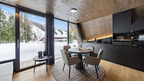 Una cocina moderna con zona de comedor, ventanas amplias y vistas a una montaña nevada.