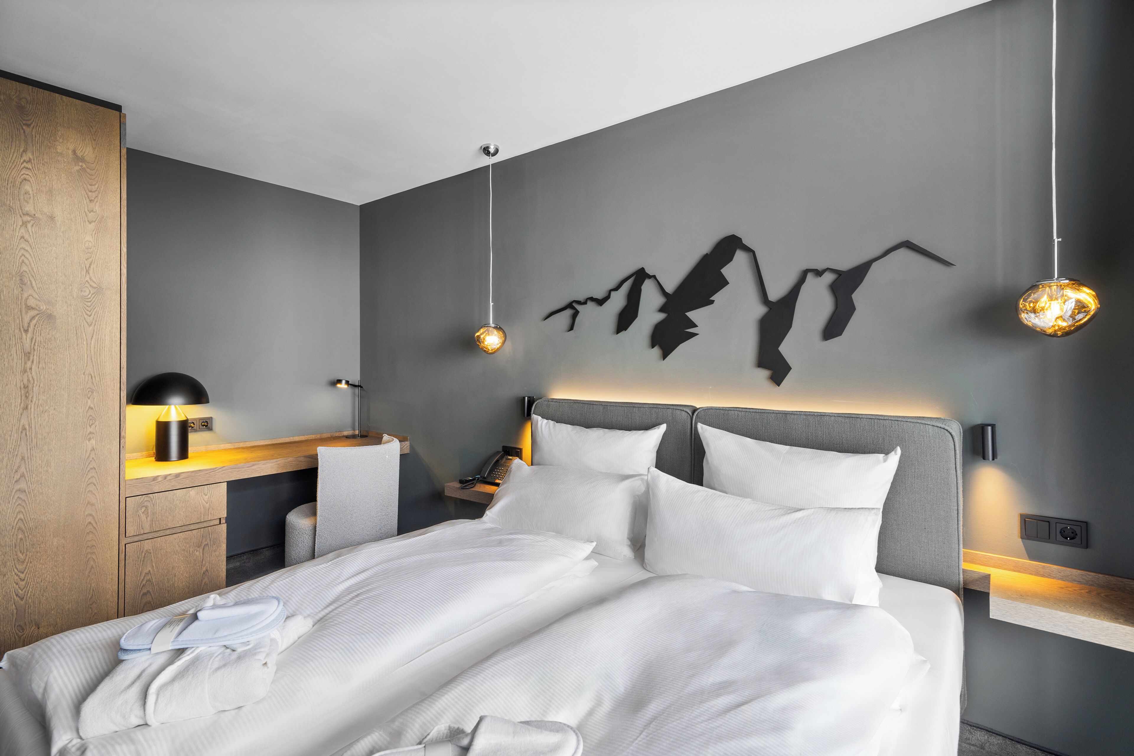 Una habitació d'hotel moderna amb un llit gran, taules de nit, un escriptori i una làmpada penjada a la paret.