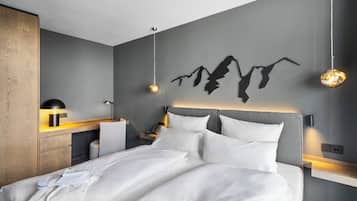 Una habitació d'hotel moderna amb un llit gran, taules de nit, un escriptori i una làmpada penjada a la paret.