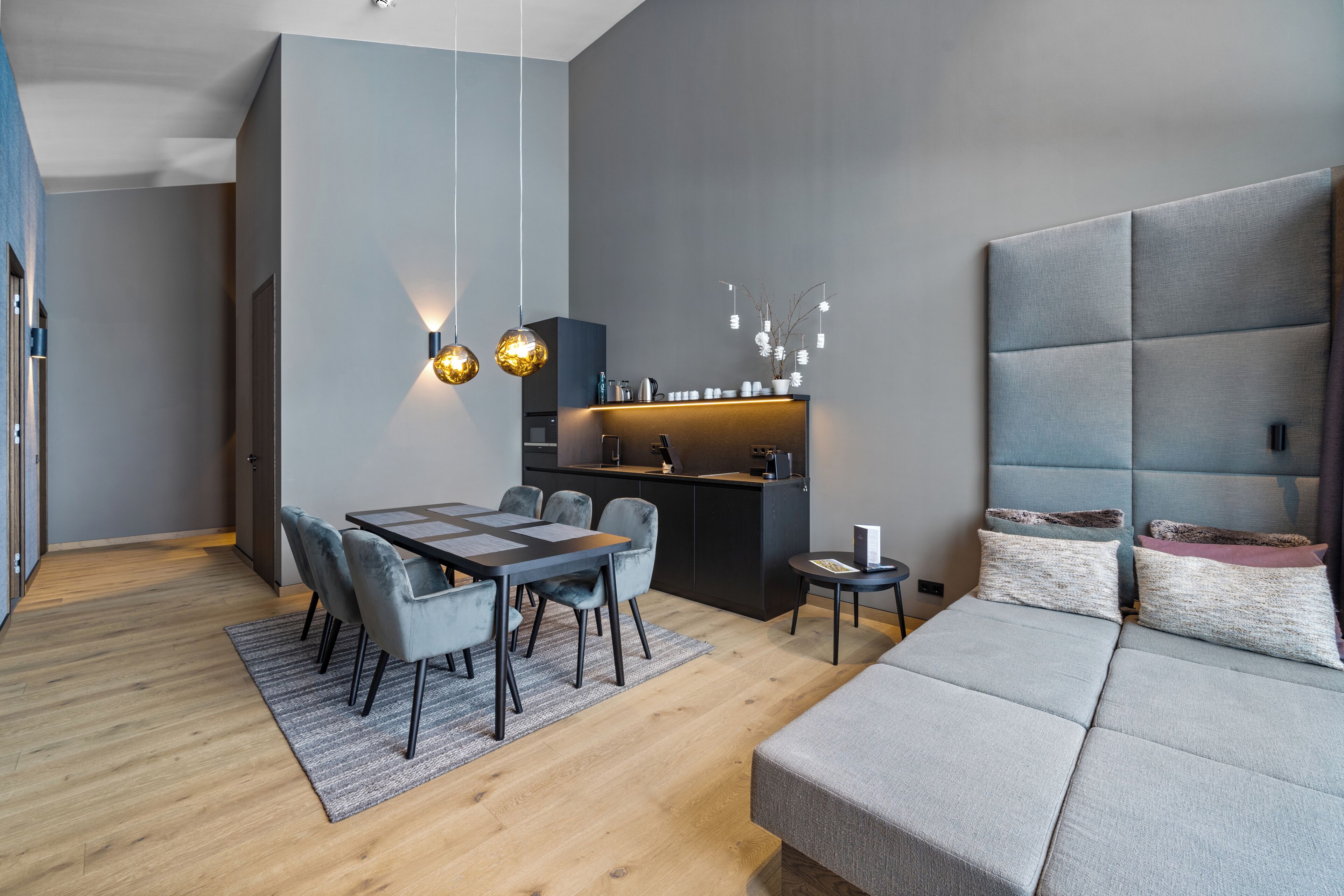 A modern living room with a sofa, dining table, chairs, a kitchen area, and pendant lights.