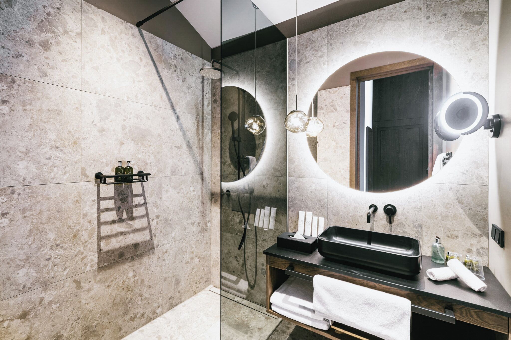 A modern bathroom with a large mirror, a black sink, and a glass shower enclosure.