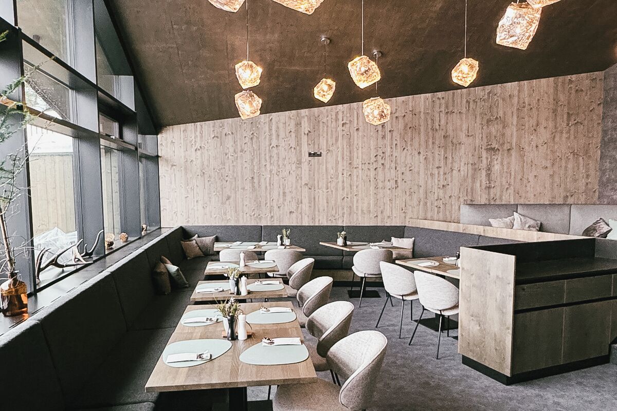 A modern restaurant with wooden tables and chairs, a bar area, and pendant lighting.