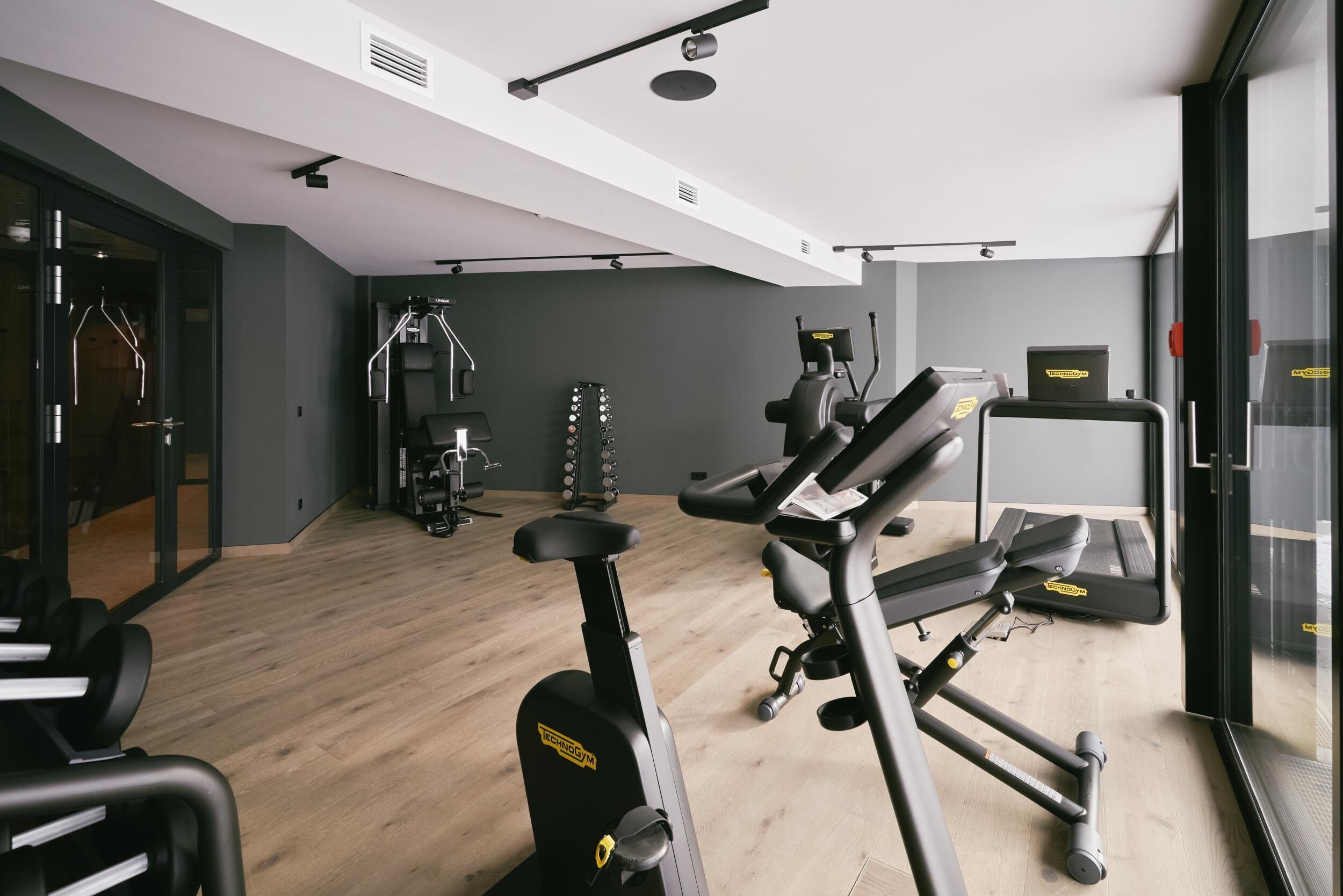 A gym with exercise equipment, a wooden floor, and a glass wall.