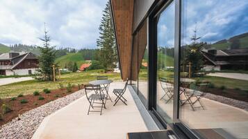 A modern building with large windows, outdoor seating, and a view of a green landscape.